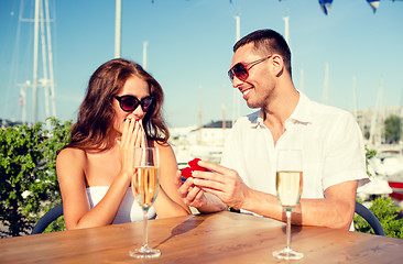 Image showing smiling couple with champagne and gift at cafe