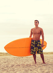 Image showing smiling young man with surfboard on beach