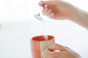 Image showing close up of woman hands adding sugar to tea cup