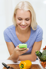 Image showing smiling woman with smartphone cooking vegetables