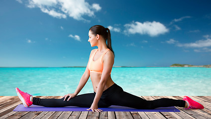 Image showing smiling woman doing splits on mat over sea