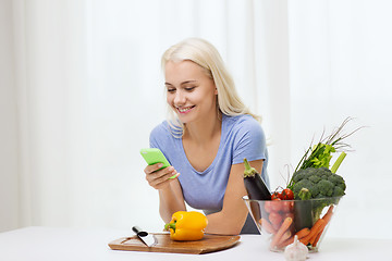 Image showing smiling woman with smartphone cooking vegetables