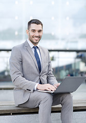 Image showing smiling businessman working with laptop outdoors