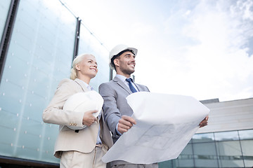 Image showing smiling businessmen with blueprint and helmets