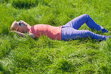 Image showing Young man in orange lying on the green grass