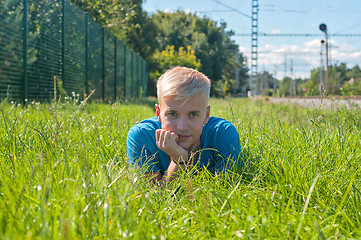 Image showing Young man in blue t-shirt lying on the green grass