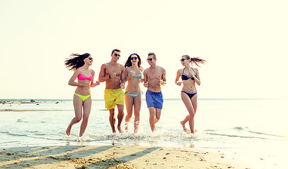 Image showing smiling friends in sunglasses running on beach