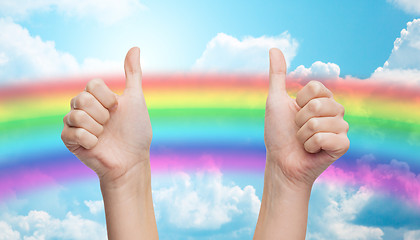 Image showing hands showing thumbs up over rainbow in blue sky