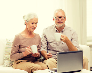 Image showing happy senior couple with laptop and cups at home