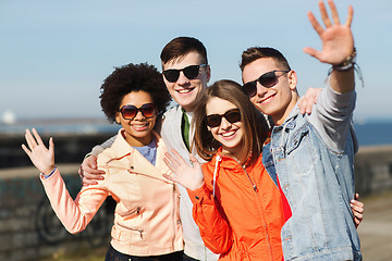 Image showing happy teenage friends in shades waving hands