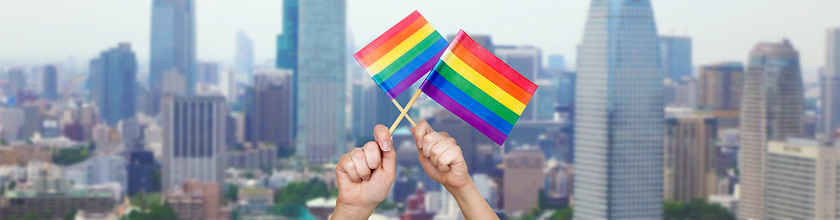Image showing hands holding rainbow flags over city background