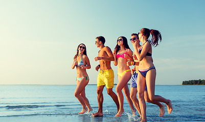 Image showing smiling friends in sunglasses running on beach