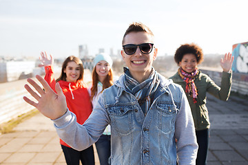 Image showing happy teenage friends waving hands on city street