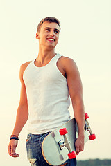 Image showing smiling teenage boy with skateboard outdoors