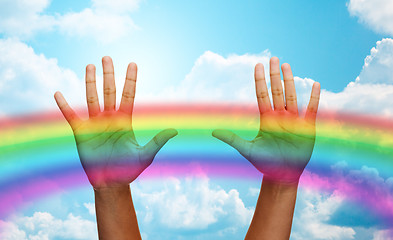 Image showing palms of human hands over rainbow in blue sky