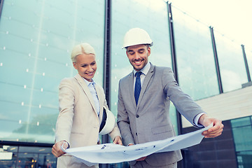 Image showing smiling businessmen with blueprint and helmets