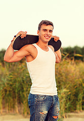 Image showing smiling teenage boy with skateboard outdoors