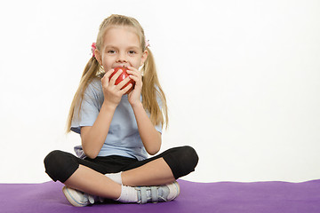 Image showing Cheerful girl eating an apple sitting on sport mat