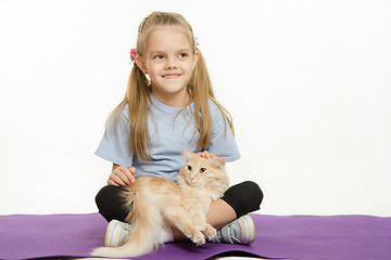 Image showing Cheerful girl sitting on a rug with cat