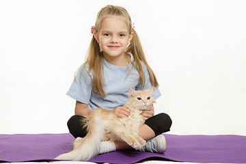 Image showing Cheerful girl sitting a rug and stroked the cat on her lap