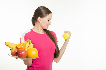 Image showing Girl athlete dumbbell raises his hand and other holding a fruit