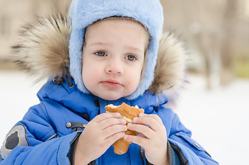 Image showing The girl eats a bun in street in winter