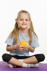 Image showing Cheerful girl sitting with orange on the sports rug