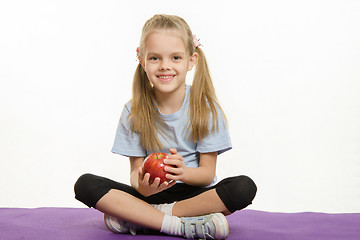 Image showing Six year old girl sitting on a rug with an apple hands