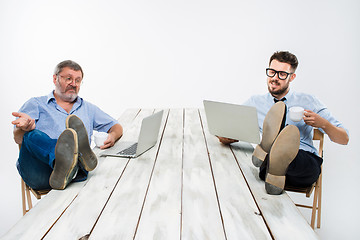 Image showing The two businessmen with legs over table working on laptops