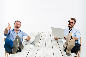 Image showing The two businessmen with legs over table working on laptops