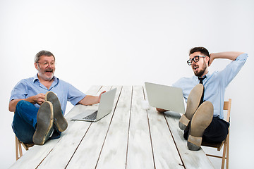 Image showing The two businessmen with legs over table working on laptops