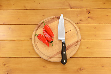 Image showing Three red peppers with a knife on a chopping board 