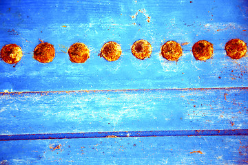 Image showing red  stripped paint in   blue wood door and rusty nail