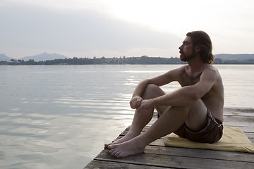 Image showing Young man sitting at a bridge in evening light