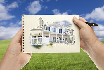 Image showing Hands Holding Paper With House Drawing Over Empty Grass Field