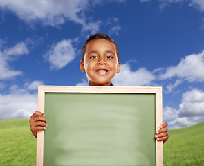 Image showing Happy Hispanic Boy In Grass Field Holding Blank Chalk Board