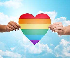 Image showing human hands with rainbow heart shape over blue sky