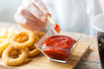 Image showing close up of hand dipping french fries into ketchup