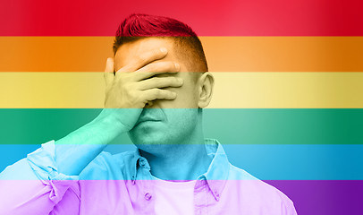 Image showing gay covering his face by hand over rainbow flag
