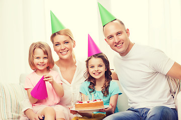 Image showing smiling family with two kids in hats with cake