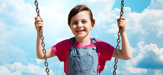 Image showing happy little girl swinging on swing over blue sky