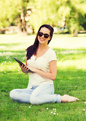 Image showing smiling young girl with tablet pc sitting on grass