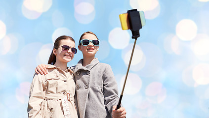 Image showing happy girls with smartphone selfie stick over blue