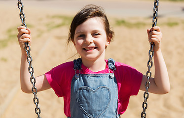 Image showing happy little girl swinging on swing at playground