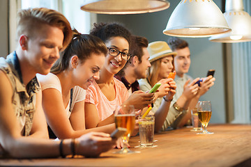 Image showing happy friends with smartphones and drinks at bar