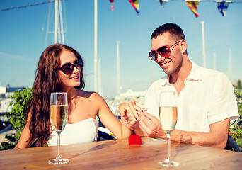 Image showing smiling couple with champagne and gift at cafe