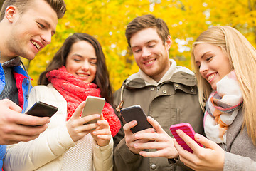 Image showing smiling friends with smartphones in autumn park