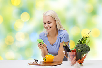 Image showing smiling woman with smartphone cooking vegetables