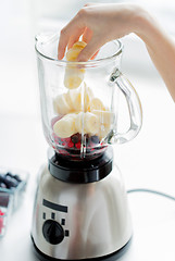Image showing close up of woman hand adding fruits to blender