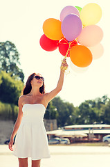 Image showing smiling young woman in sunglasses with balloons